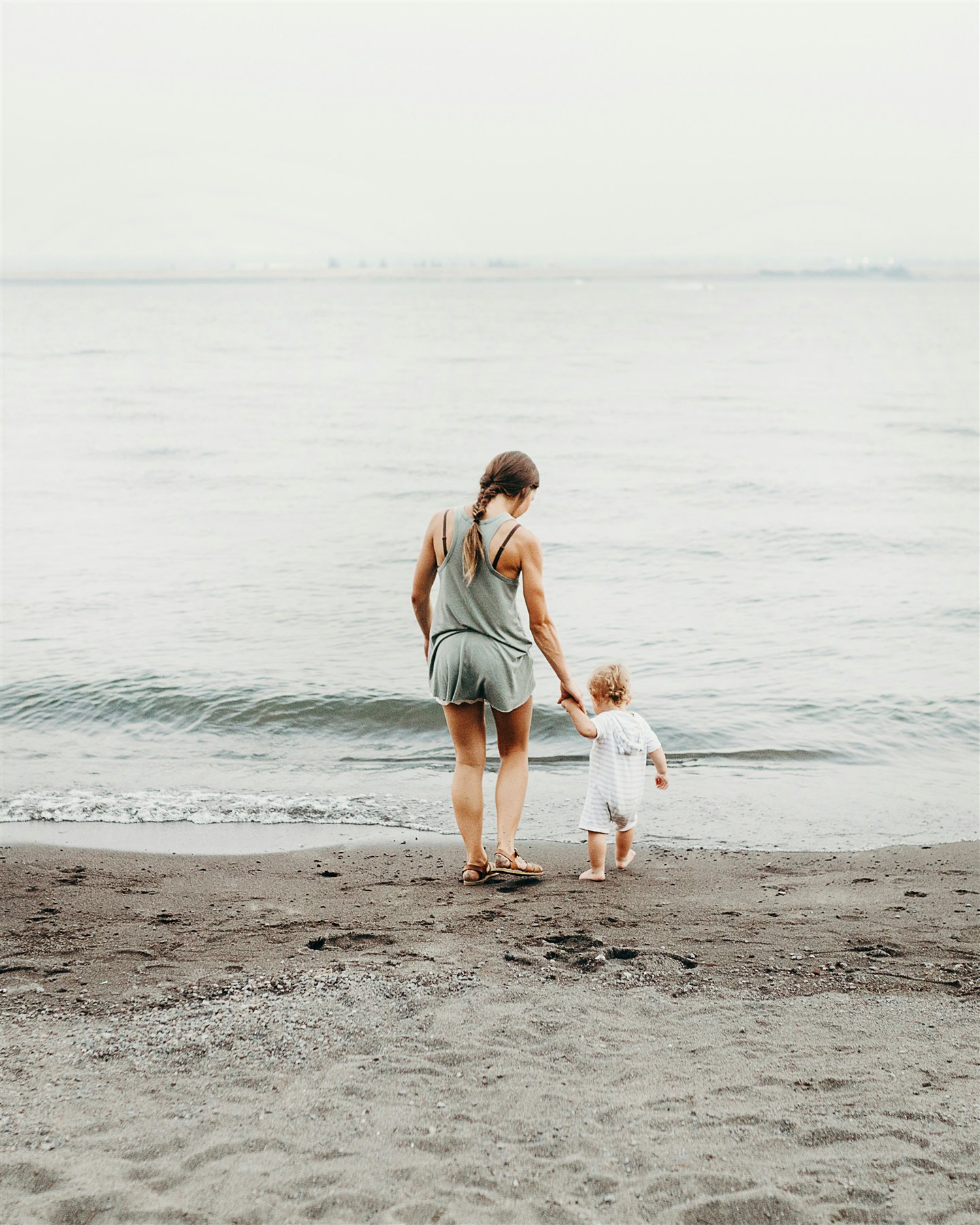 A mother and toddler walking hand in hand along the shore