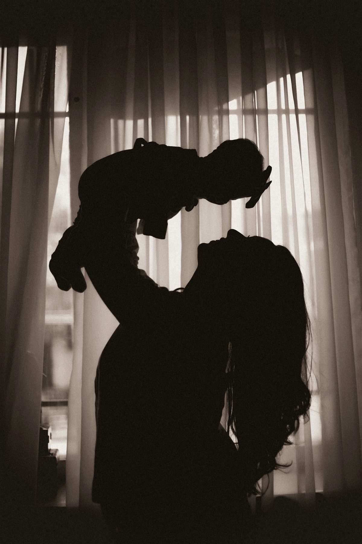 Silhouette of a mother lifting her baby up in the light of a window