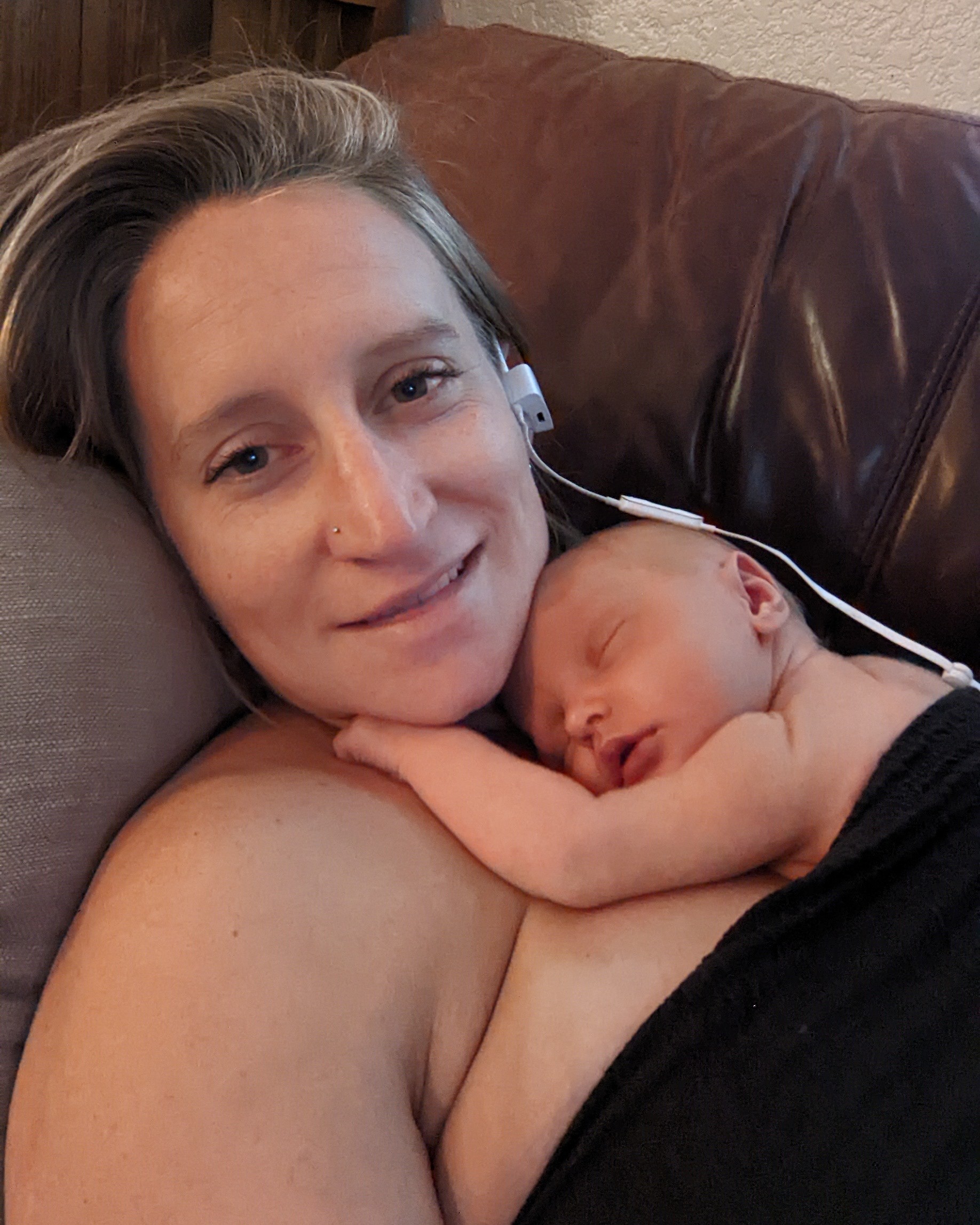 Ellen resting her cheek against her sleeping newborn on a brown leather couch