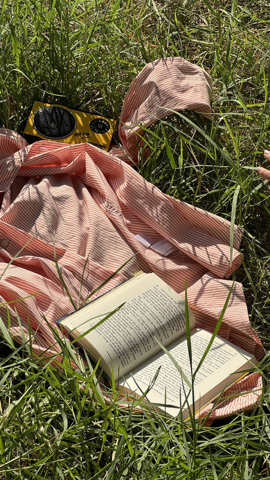 A striped shirt, book, and vintage radio laid out in the grass for a quiet moment outside