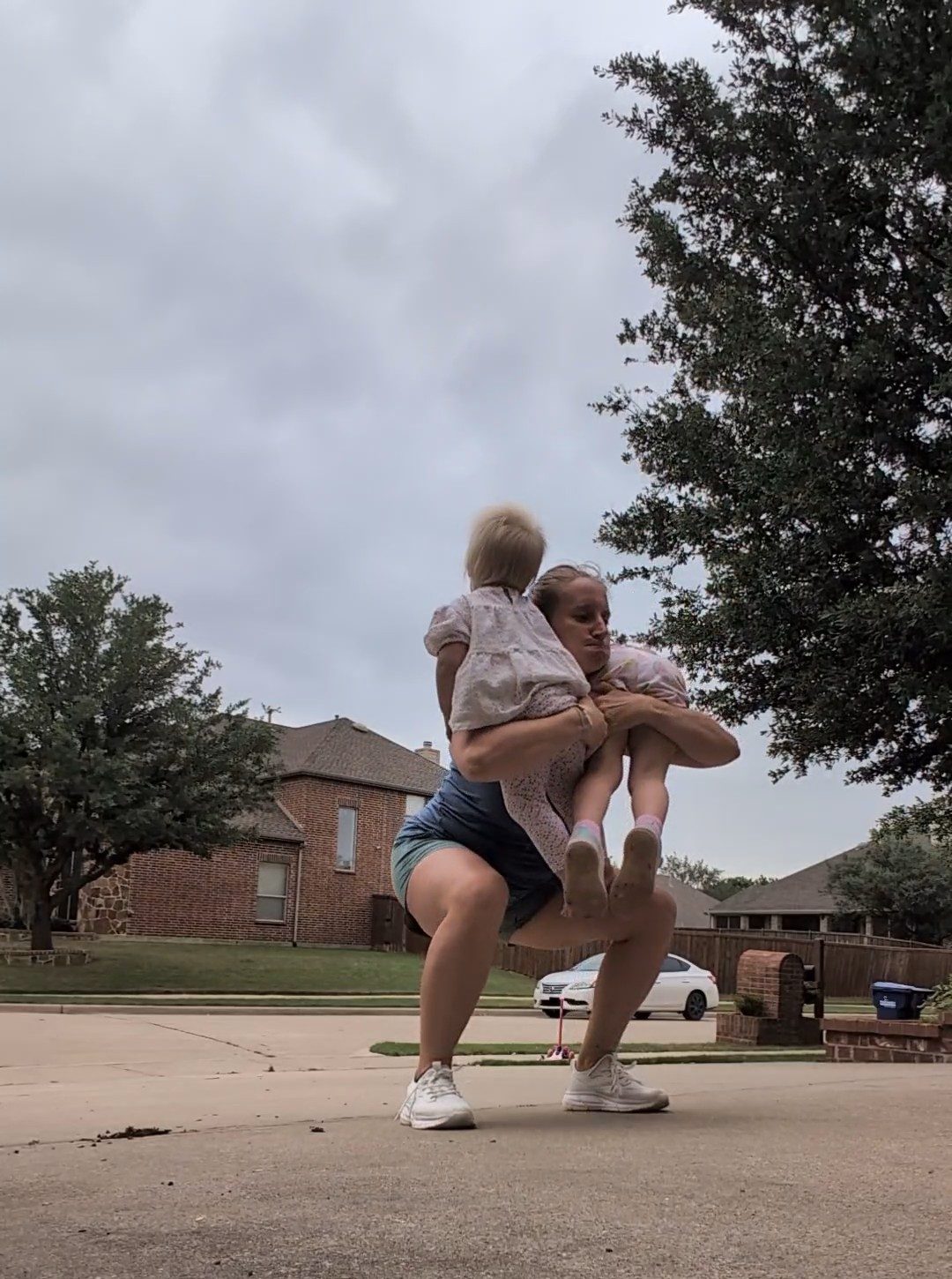 A mother squatting while holding her two children outdoors, building strength